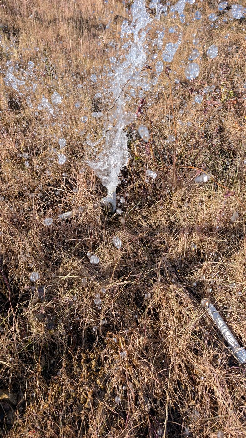 Broken irrigation riser spraying water across a landscape